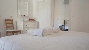 A neatly made bed with rolled towels, a wooden chair, a white dresser, and a mirror on the wall.
