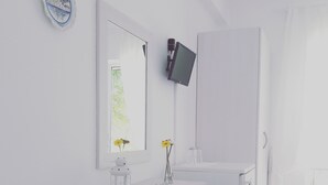 A modern bathroom with a white vanity, a mirror, a mounted TV, and a small decorative item on the counter.