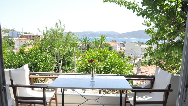 A balcony with a table and two chairs, overlooking a scenic view of a coastal town and mountains.