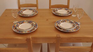 A wooden dining table with four chairs, each with a colorful plate and a wine glass.