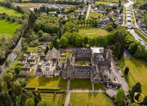 Ein Luftbild eines großen, historischen Anwesens mit einem zentralen, schlossartigen Bau, umgeben von gepflegten Gärten und Wohnhäusern.