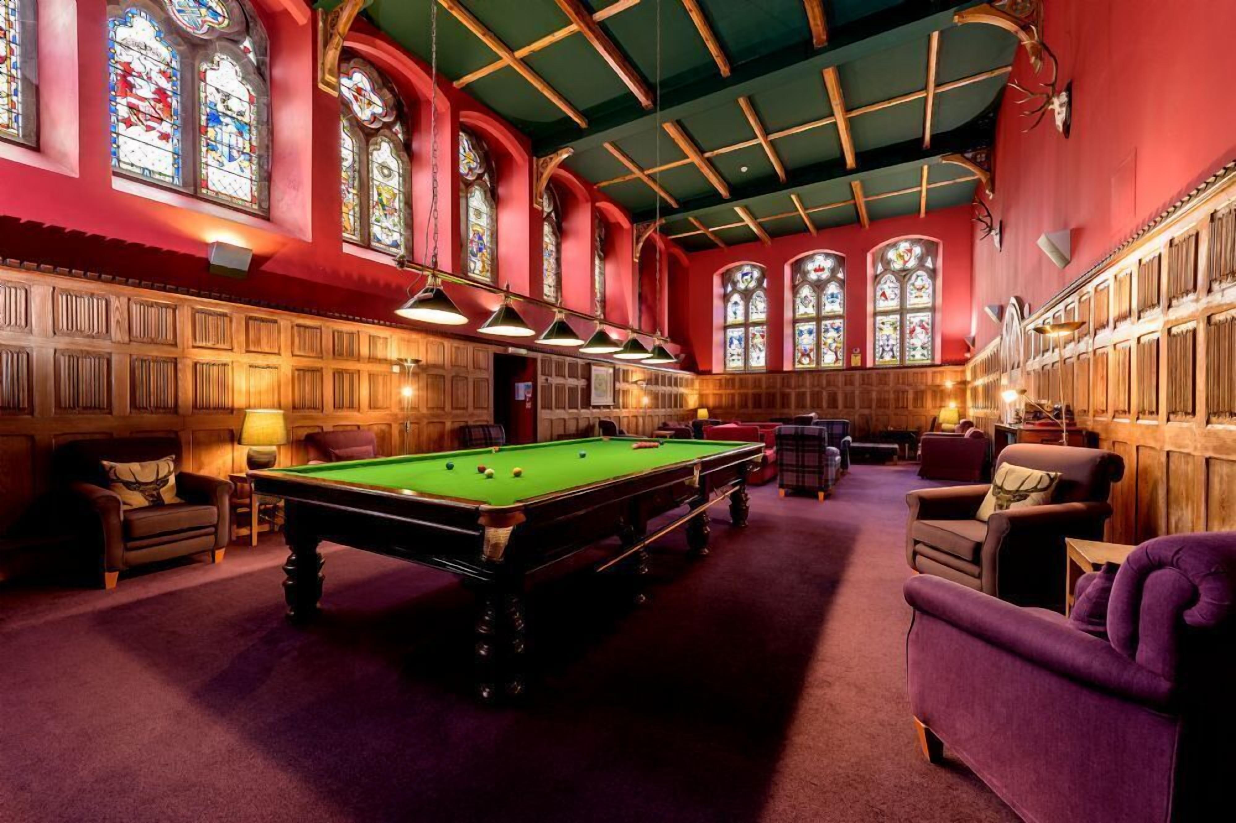 Een biljartkamer met een pooltafel, houten lambrisering en glas-in-loodramen.