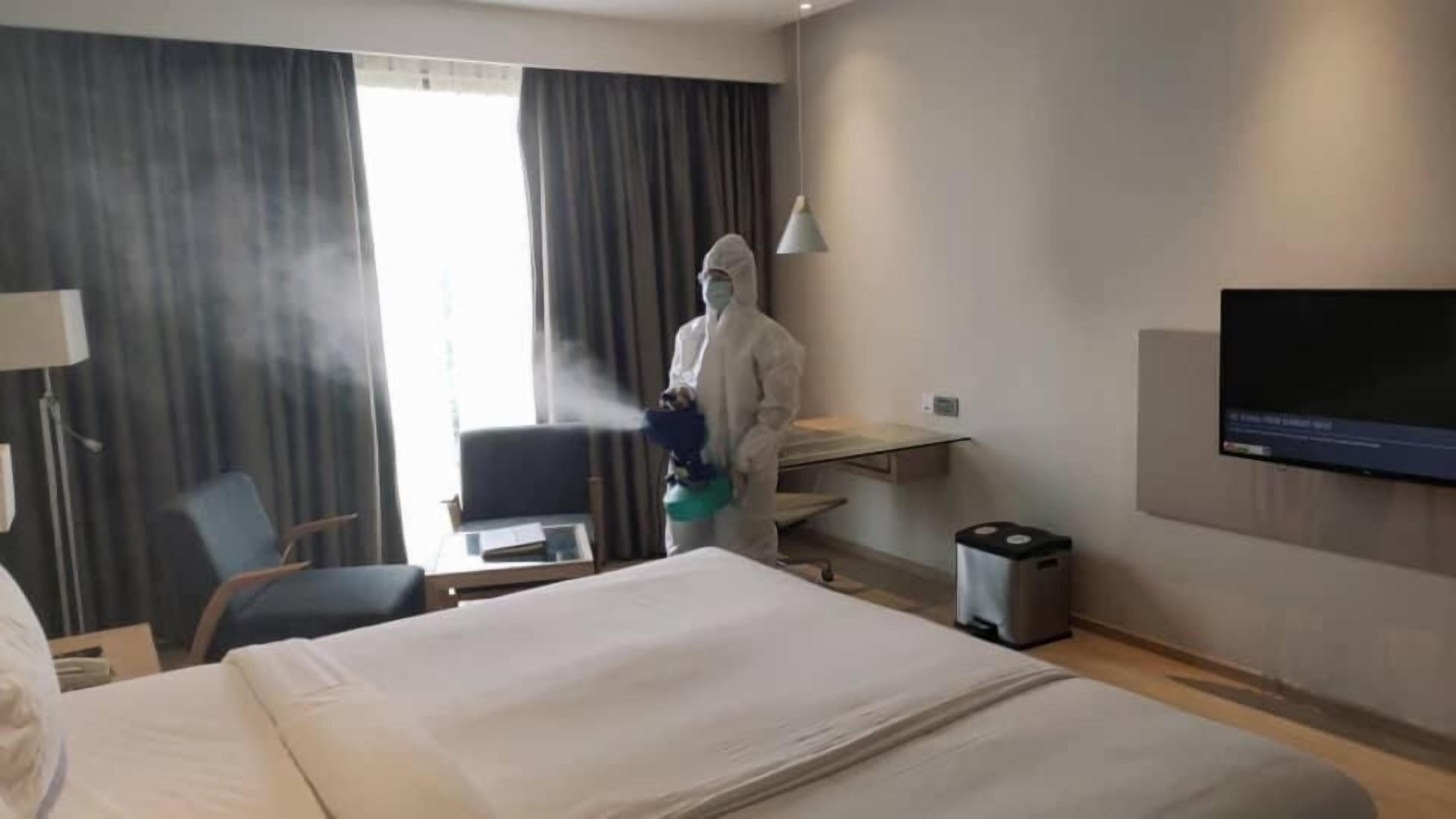 A hotel room with a bed, a desk, a chair, a TV, and a window with curtains.