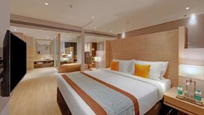 Une chambre d’hôtel avec un grand lit, une table de chevet avec une lampe, une télévision et une salle de bain visible au fond.