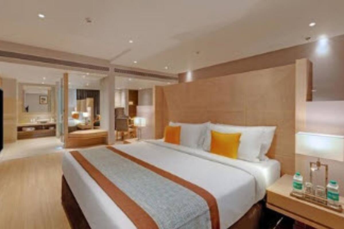 Une chambre d’hôtel avec un grand lit, une table de chevet avec une lampe, une télévision et une salle de bain visible au fond.