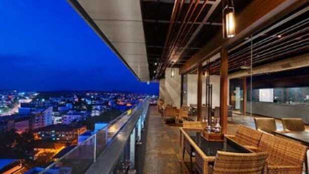 Un bar situé sur un toit, avec des meubles en osier et une vue sur la ville au crépuscule.