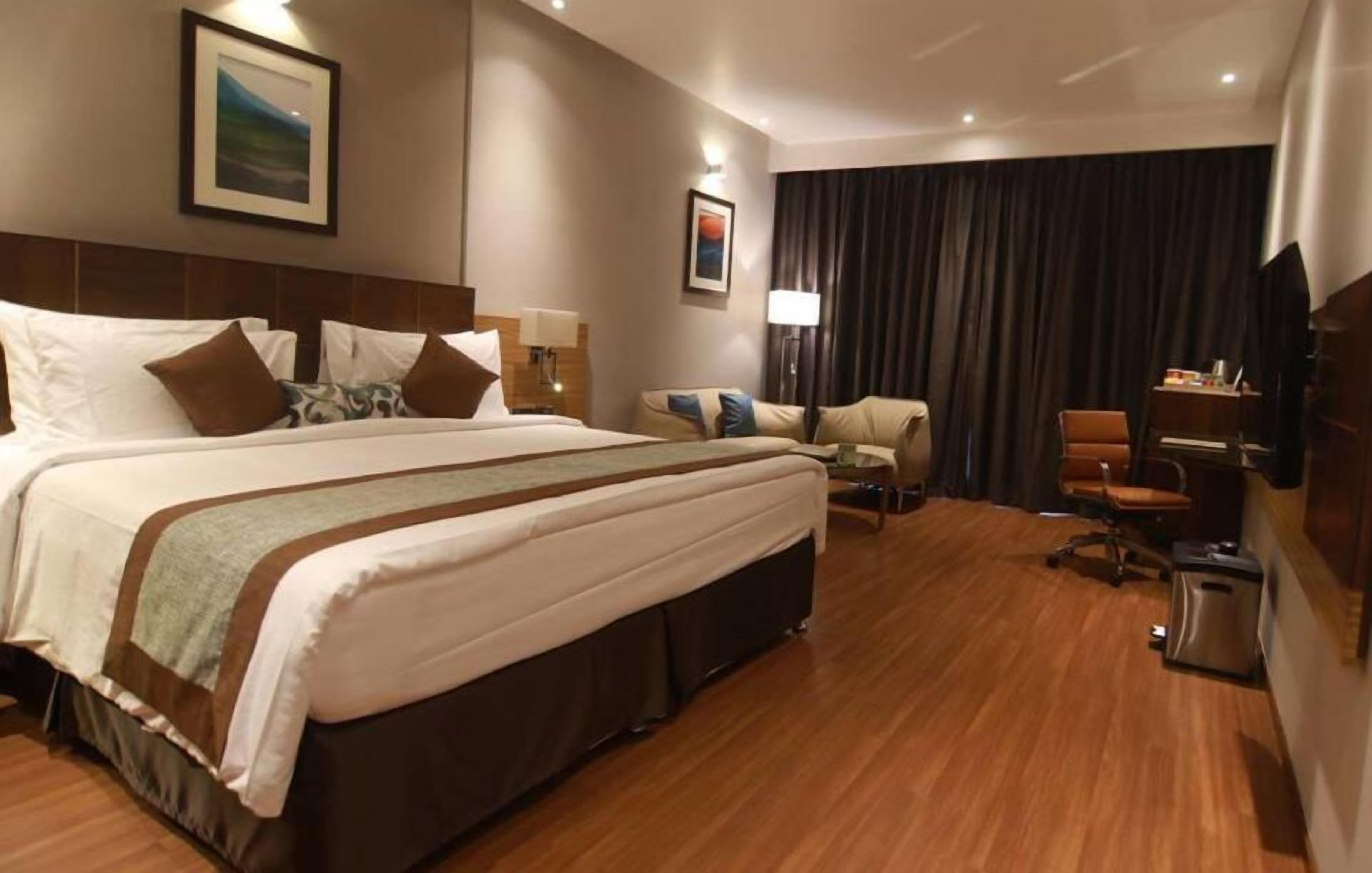 Een hotelkamer met een groot bed, een bureau, een stoel, een televisie en een raam met gordijnen.