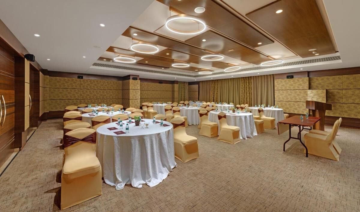 A conference room with multiple round tables, beige chairs, and a carpeted floor.