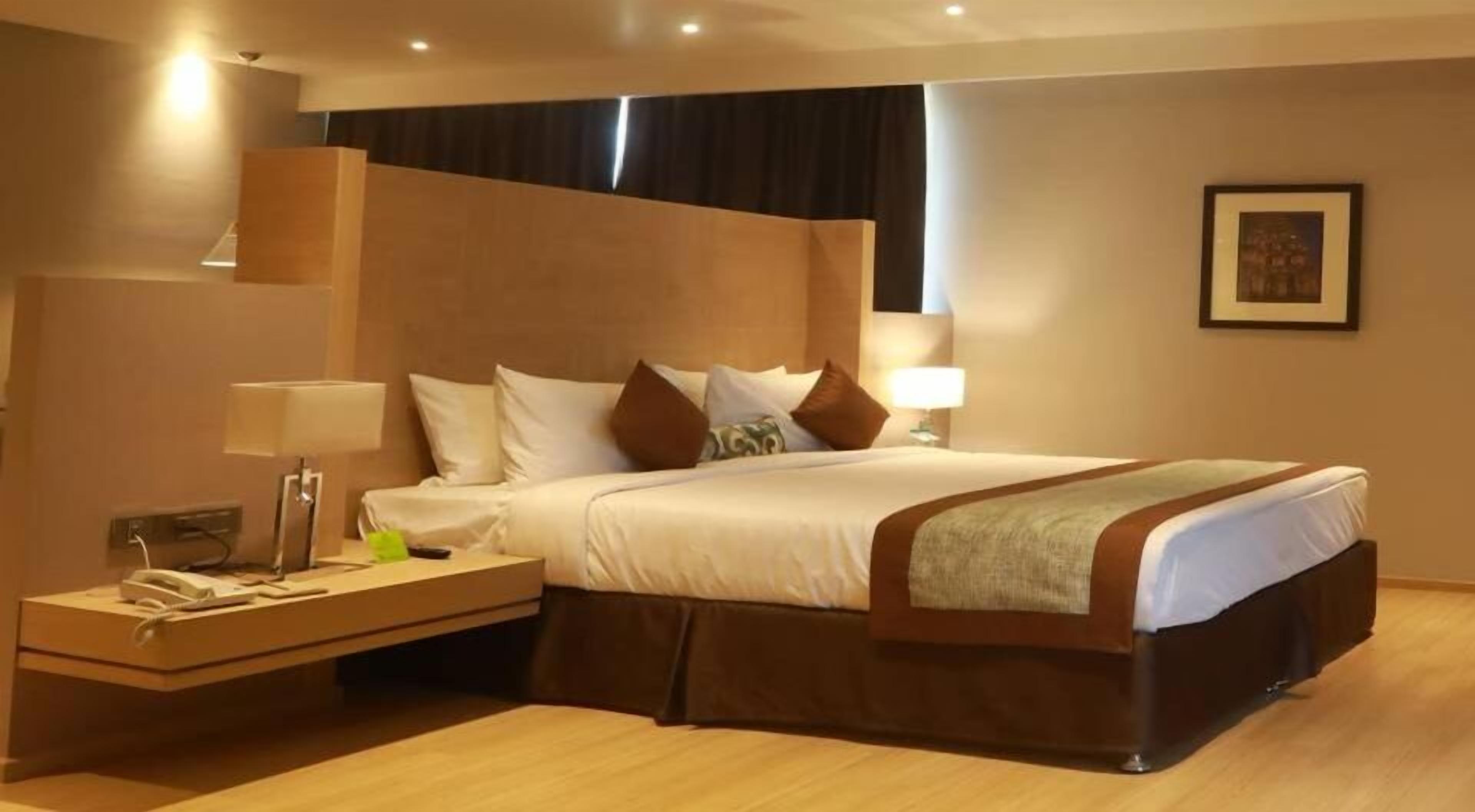 A hotel room with a large bed, bedside tables, a lamp, and a framed picture on the wall.