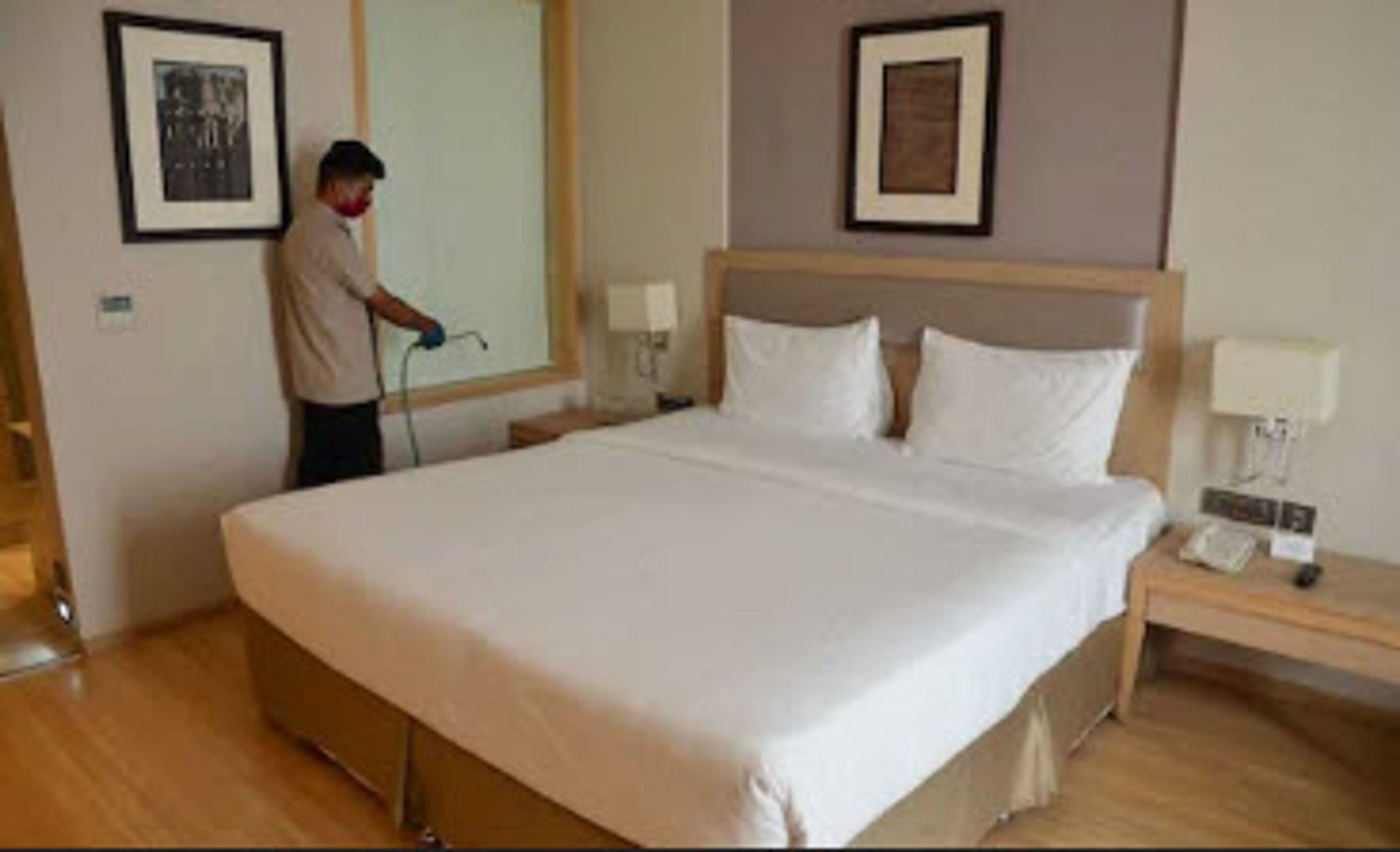 A hotel room with a large bed, a nightstand, a lamp, and two framed pictures on the wall.