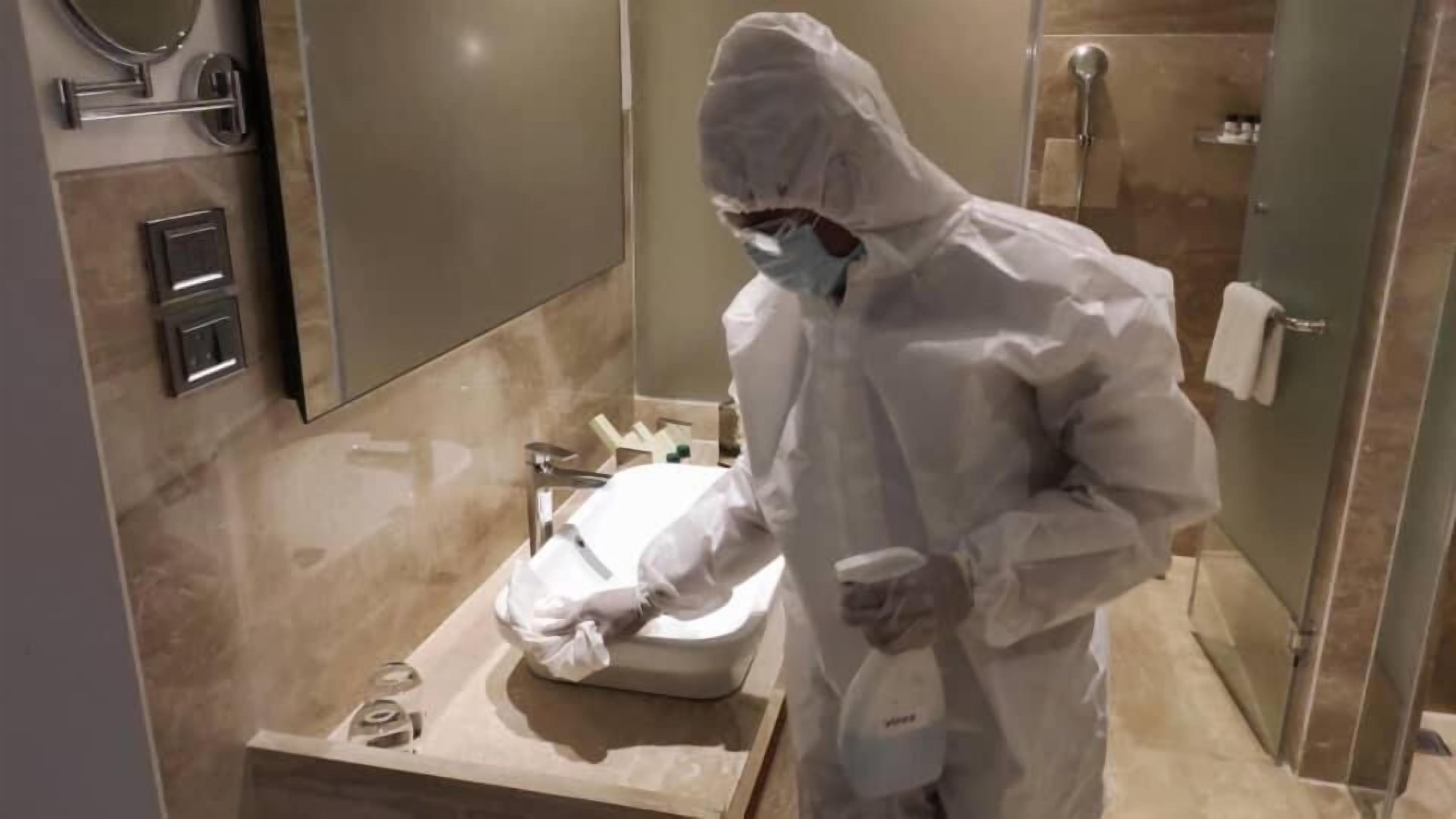 Una persona con tuta protettiva in un bagno con lavandino, specchio e doccia.