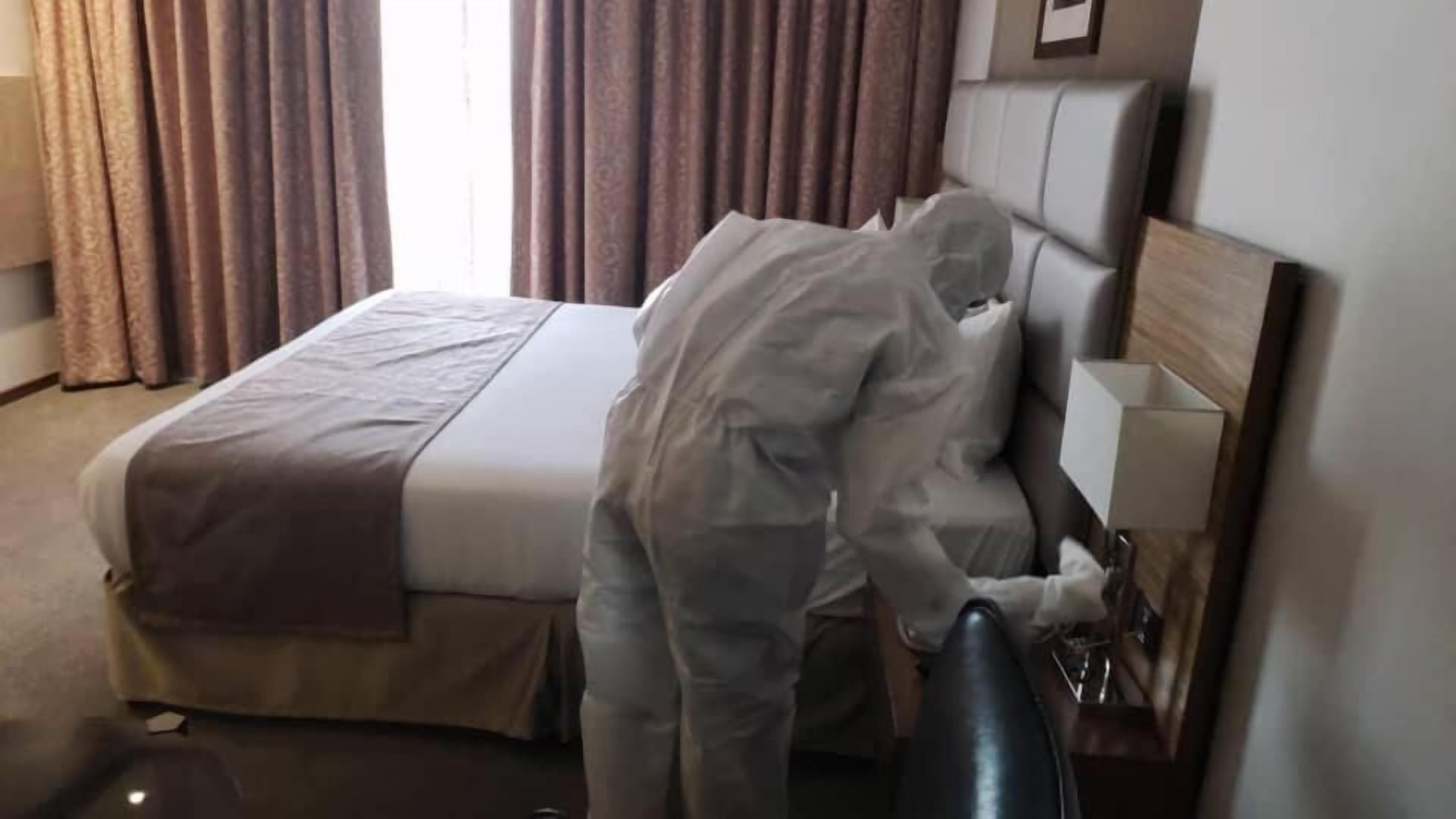 A hotel room with a bed, curtains, a bedside table, and a lamp.