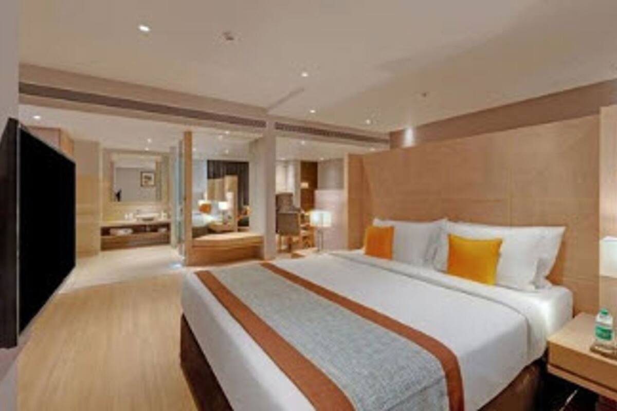 Une chambre d’hôtel avec un grand lit, une table de chevet avec une lampe, une télévision et une salle de bain visible au fond.