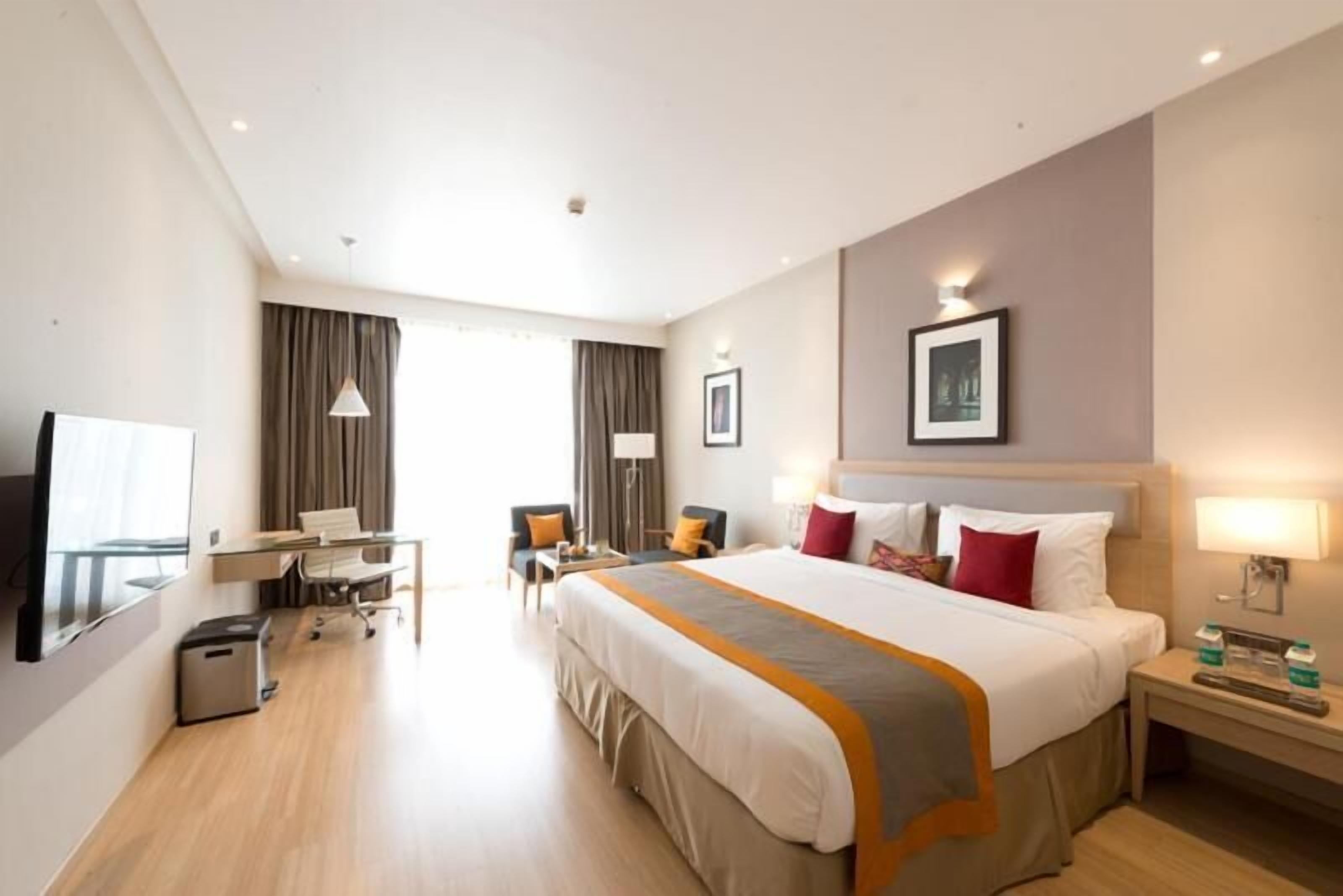 Een hotelkamer met een groot bed, een bureau, een stoel, een televisie en een schilderij aan de muur.
