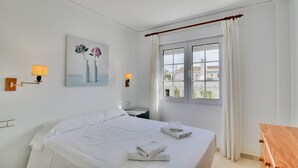 Une chambre d’hôtel avec un lit, deux lampes de chevet, une fenêtre avec des rideaux, une petite table de chevet et un tableau au mur.
