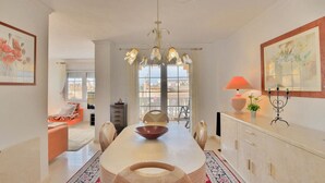 Un espace repas comprenant une grande table, des chaises, un lustre et une vue par la fenêtre.