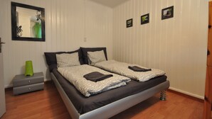 Una cama doble con ropa de cama estampada, una mesita de noche con un florero verde y un espejo en la pared.