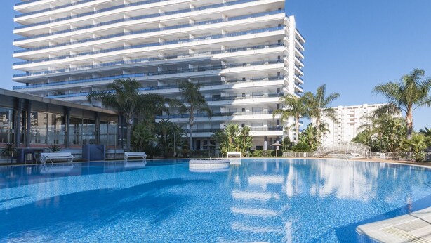 A modern hotel with a large pool area, palm trees, and a multi-story building with balconies. - ALEJANDRITA - Apartment with shared pool in Playa De Gandia and Free Wifi (Gandia)