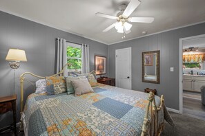 A bedroom with a large bed, a ceiling fan, a nightstand, a lamp, a window with curtains, and a door leading to a bathroom. - Perfect mountain cottage ☎ Fire pit ☎ Gas Fireplace ☎ Screened Porch ☎ Secluded (Townsend)