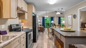 A kitchen with wooden cabinets, a stove, and a dining area with a table and chairs. - Perfect mountain cottage ☎ Fire pit ☎ Gas Fireplace ☎ Screened Porch ☎ Secluded (Townsend)