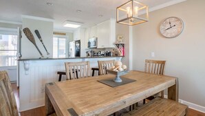 A dining area with a wooden table and benches, a chandelier, and a clock on the wall. - Ocean Dunes 1701 (Kure Beach)