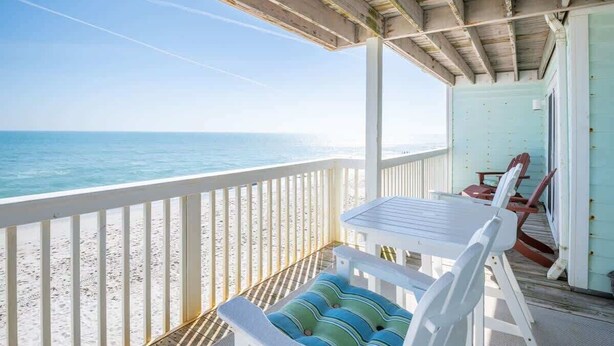 A covered outdoor area with a table and chairs, a view of the ocean, and a sandy beach. - Ocean Dunes 1701 (Kure Beach)