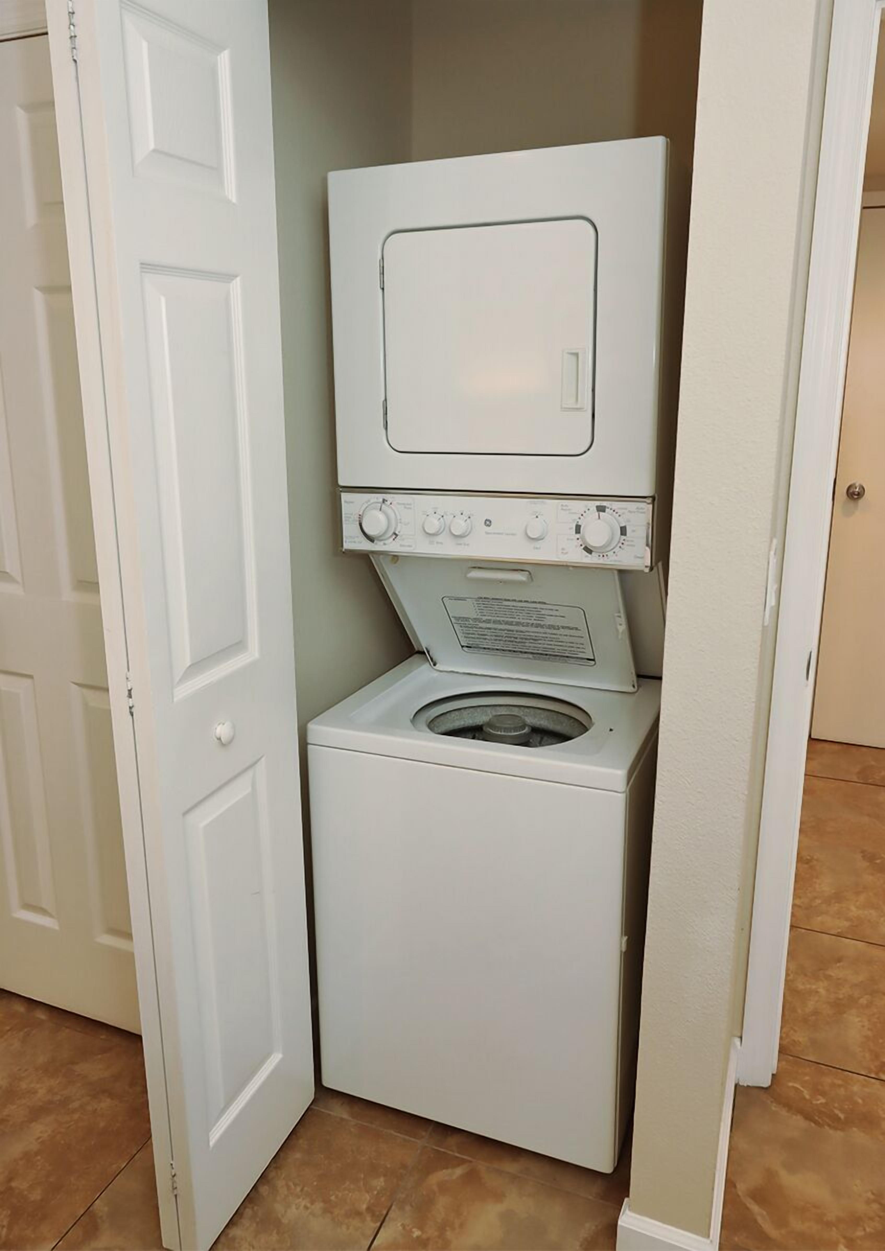 Un lavadero pequeño con lavadora y secadora de carga frontal, una puerta y piso de baldosas.