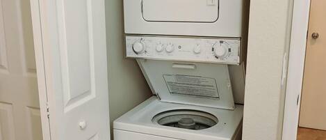 Un lavadero pequeño con lavadora y secadora de carga frontal, una puerta y piso de baldosas.
