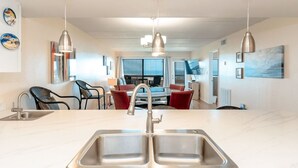 A modern kitchen with a double sink, pendant lighting, and a dining area with red chairs. - Saida II 302 - Beachfront Condo, Great Views from Balcony, Oceanfront Pools & Hot Tubs (South Padre Island)