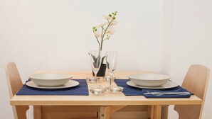 Ein Esstisch mit zwei weißen Tellern, einer Blumenvase und klaren Gläsern auf einer blauen Tischmatte.