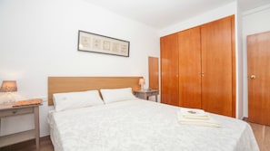 A bedroom with a bed, a nightstand, a lamp, a framed picture on the wall, and a wooden wardrobe.