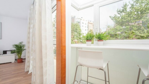 Ein modernes Wohnzimmer mit großem Fenster, einem weißen Sofa, einem kleinen Tisch und einer Topfpflanze.