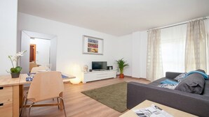 Ein modernes Wohnzimmer mit Essbereich, einem Flachbildfernseher und einer Couch mit Kissen.