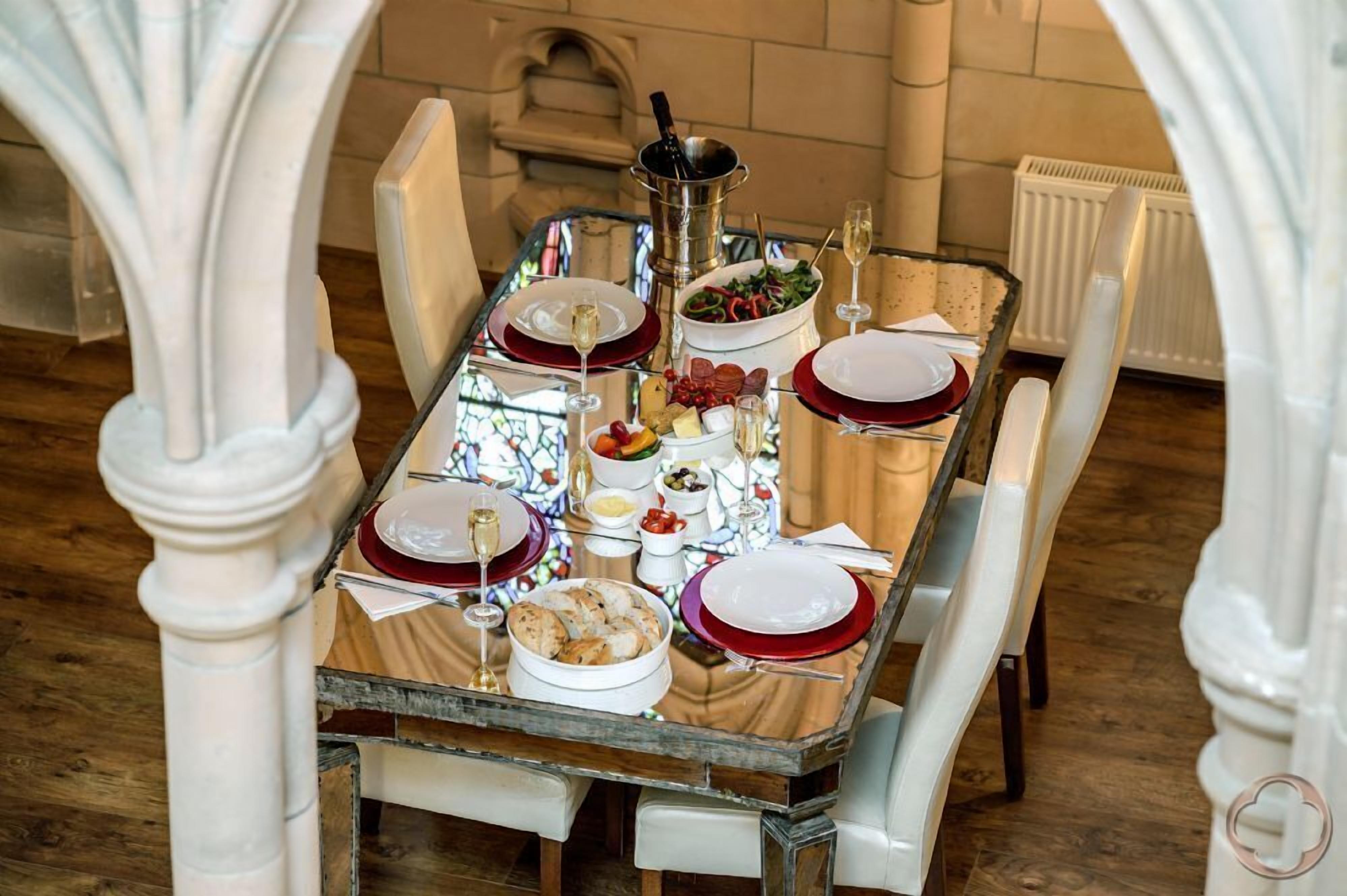 A dining table set with red and white plates, glasses, and a variety of dishes, including a salad and bread, in a room with white columns and a tiled floor.