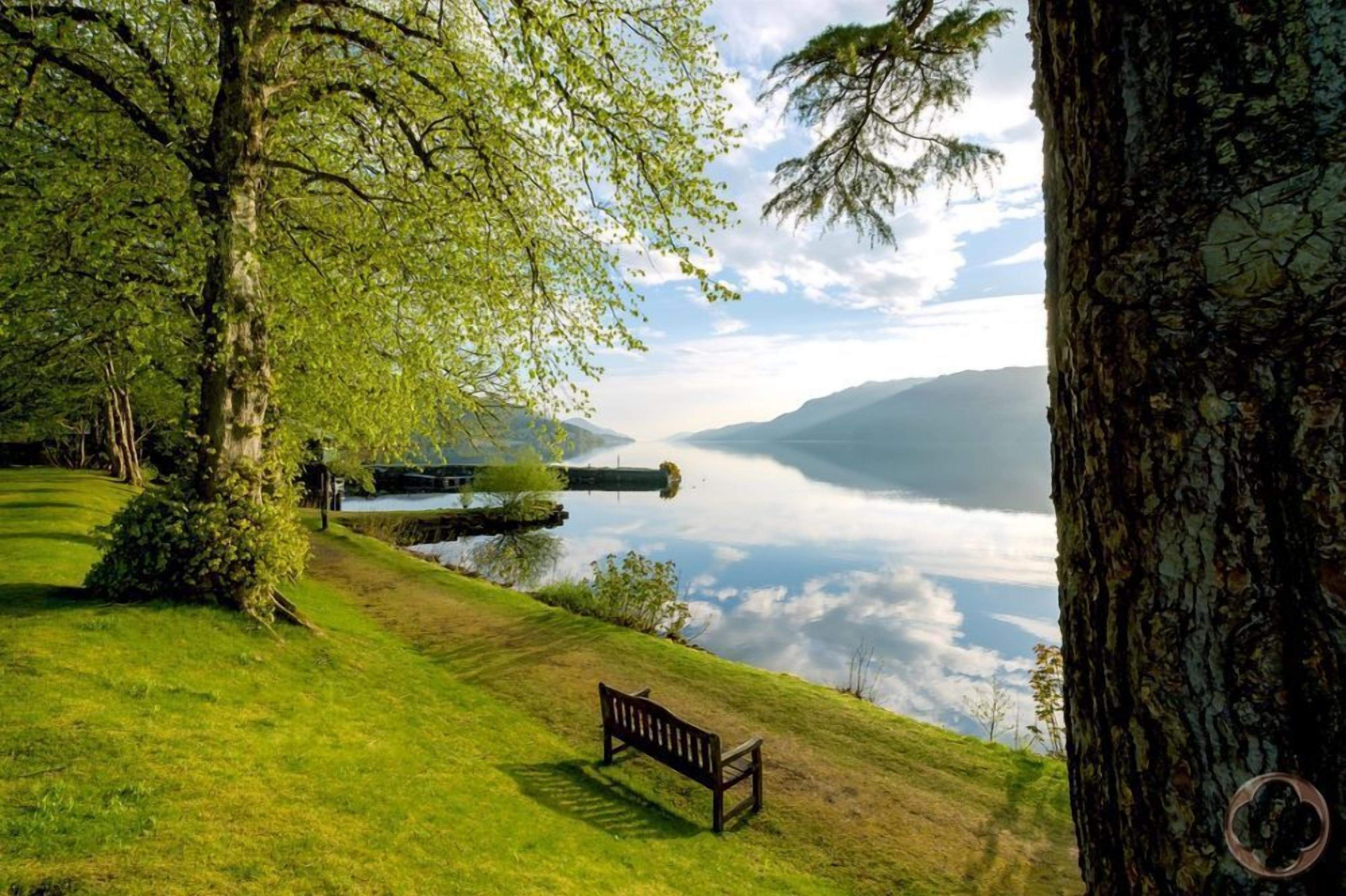 Un banc sur une colline verdoyante, d’où l’on a une vue sur un lac et, au loin, sur des montagnes.
