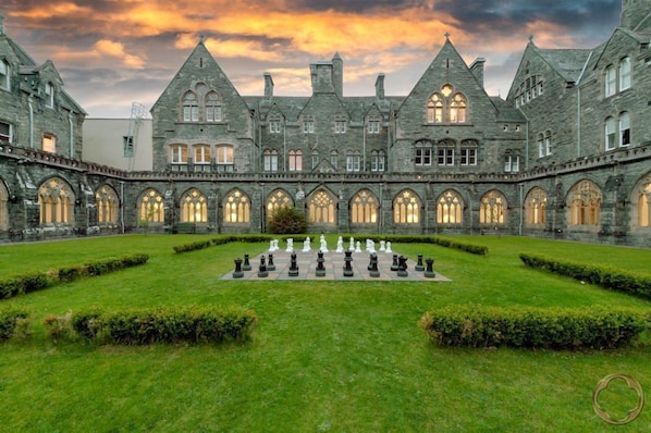 A courtyard with a chessboard, surrounded by stone buildings with arched windows and a castle-like architecture.
