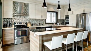 A modern kitchen with stainless steel appliances, a large island with bar stools, and pendant lighting. - Luxury cottage, panoramic view over the entire valley/Ski Resort, 24 people (Stoneham-et-Tewkesbury)