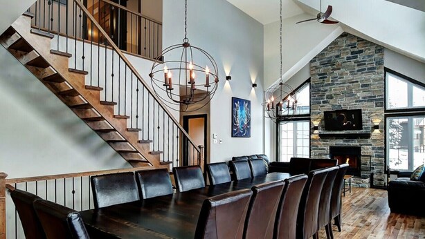 A spacious living area with a large wooden dining table, leather chairs, a stone fireplace, and a staircase with wooden railings. - Luxury cottage, panoramic view over the entire valley/Ski Resort, 24 people (Stoneham-et-Tewkesbury)