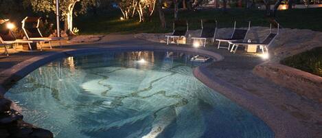 A swimming pool with lounge chairs and a stone border.