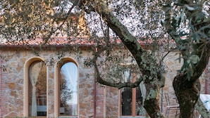Un bâtiment en pierre doté de trois fenêtres en arc de cercle, avec un arbre au premier plan.
