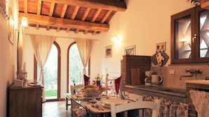 Un espace repas doté d’un plafond en bois, d’une cheminée en briques et offrant une vue à travers des fenêtres en arc de cercle.