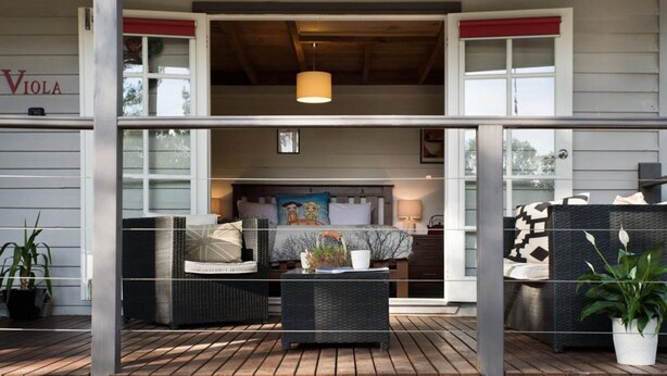 Een moderne buitenzitplaats met rieten meubilair, een houten terras en uitzicht op het interieur.