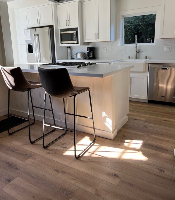 A modern kitchen with white cabinets, stainless steel appliances, and a wooden floor.