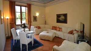 Una sala de estar con un sofá, una mesa de comedor con sillas, un televisor y un cuadro en la pared.