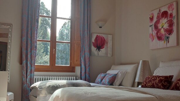 Un dormitorio con una cama grande, una ventana con cortinas, un radiador, una silla y un cuadro en la pared.
