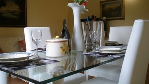 Una mesa de comedor dispuesta con platos blancos, un florero de cristal con flores y una copa de vino.