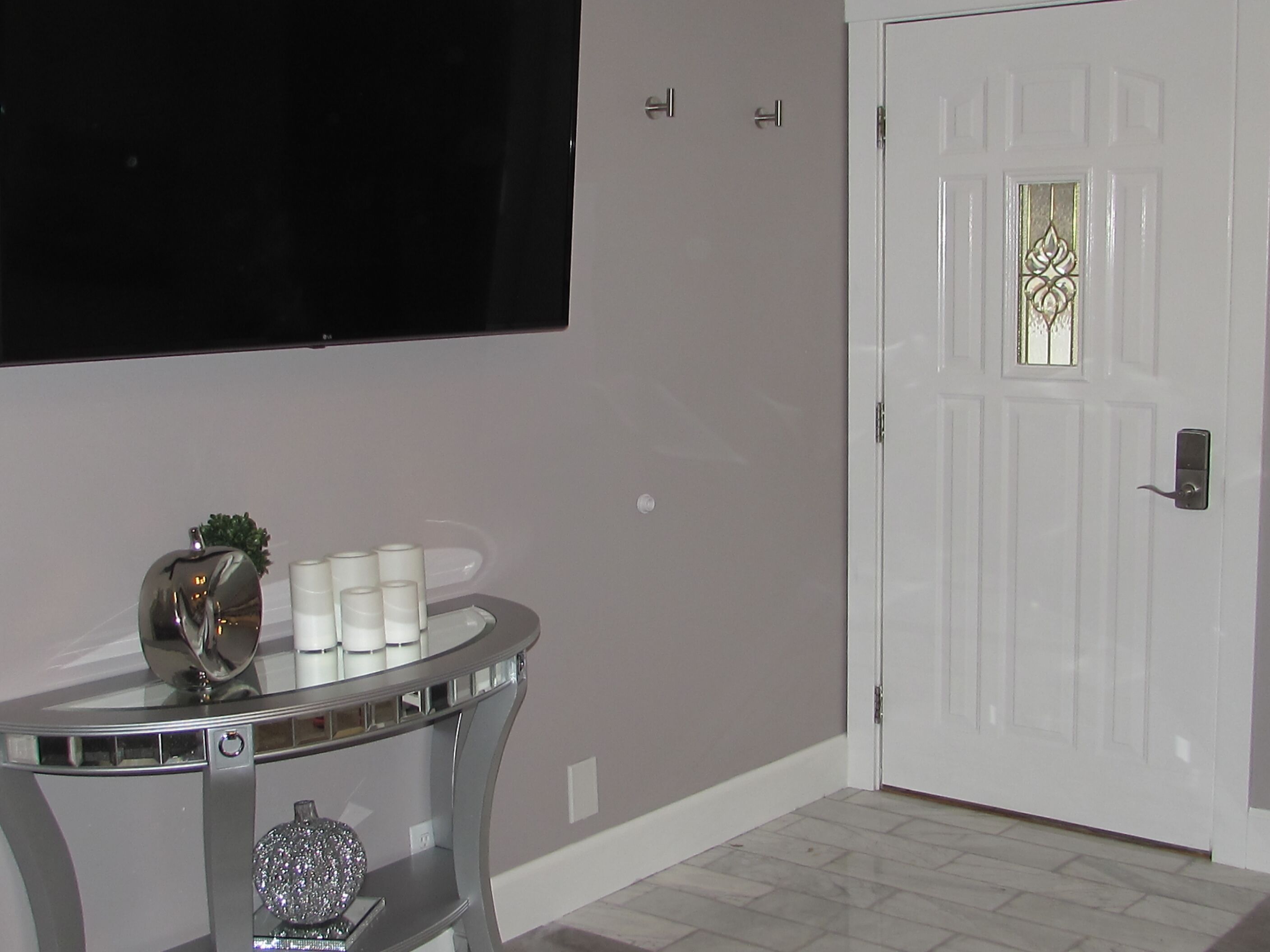 A room with a white door, a flat-screen TV mounted on the wall, and a glass table with decorative items.
