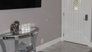 A room with a white door, a flat-screen TV mounted on the wall, and a glass table with decorative items.