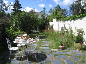 Un patio exterior con un sendero de piedra, sillas de metal y una mesa lista para una comida.