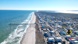 An aerial view of a coastal town with a pier extending into the ocean, a beach, and a densely packed residential area with houses and streets. - BEST DEAL IN KURE BEACH!!! FULLY RENOVATED LUXURY HOME STEPS TO THE OCEAN & PIER (Kure Beach)